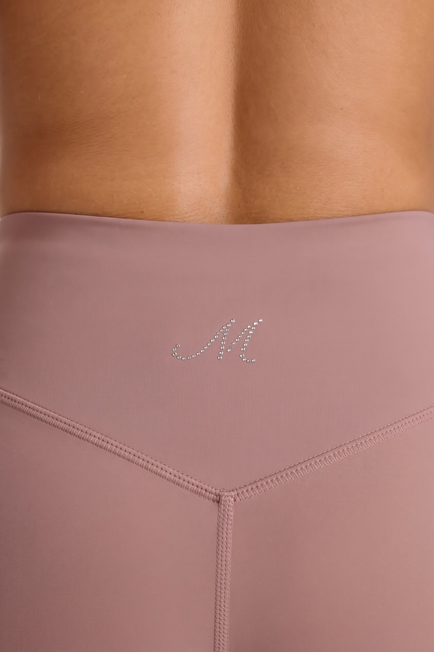 Close-up of the dusty rose shorts waistband with rhinestone M logo and V-shaped stitching