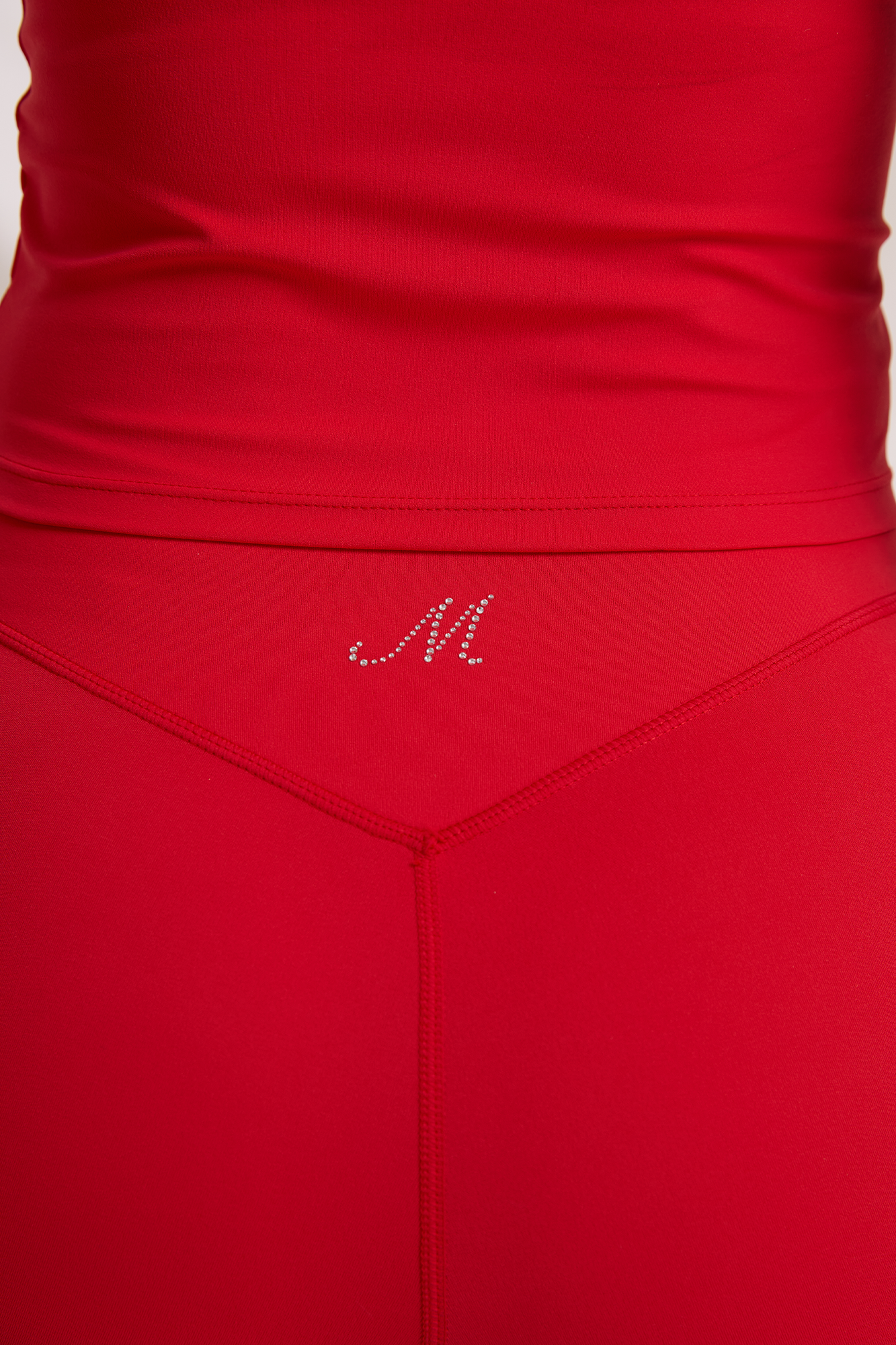 Back waistband detail of red workout shorts, showing a V-shaped seam and M logo