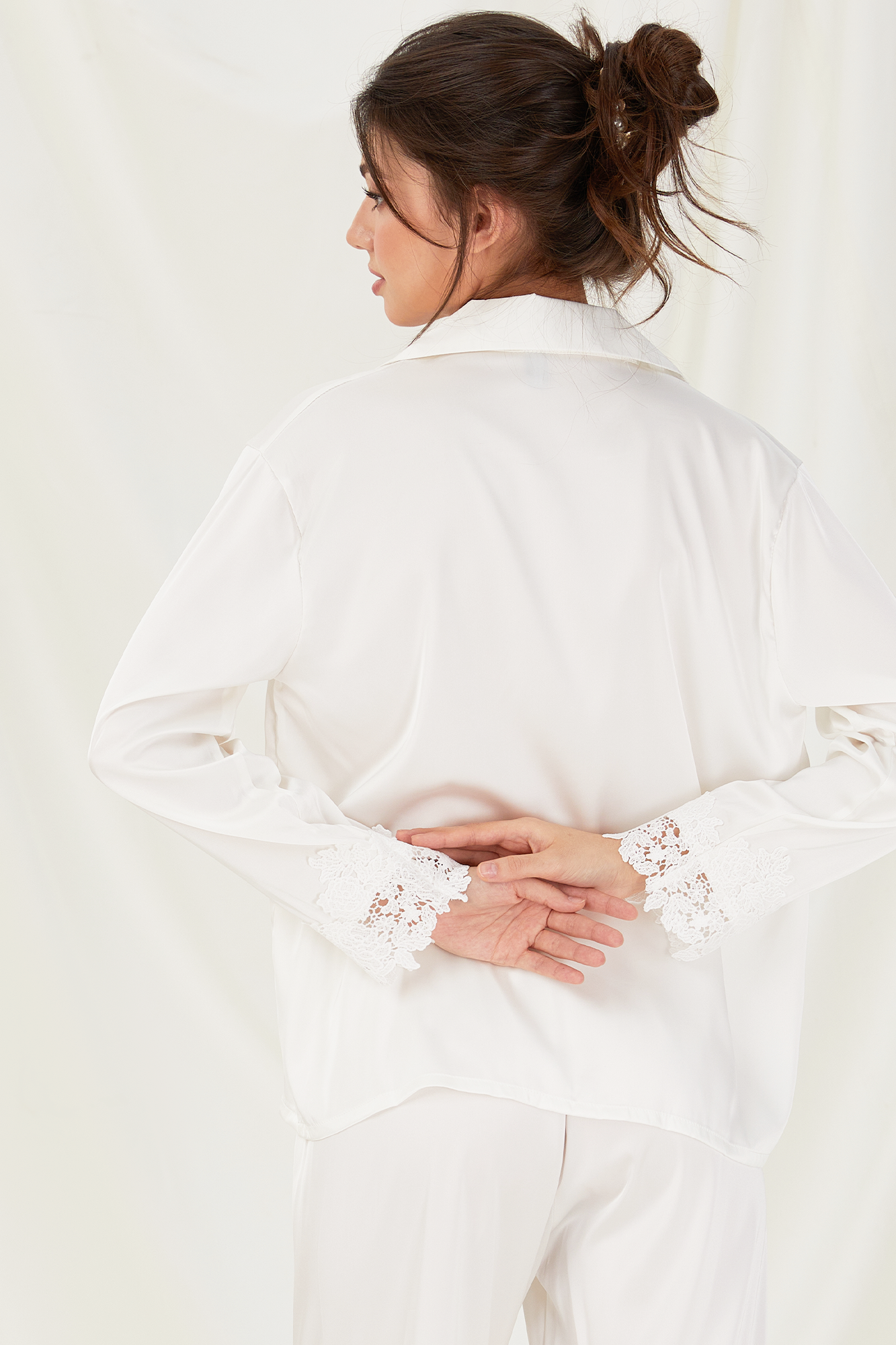 Woman wearing a white blouse with lace details on a plain background