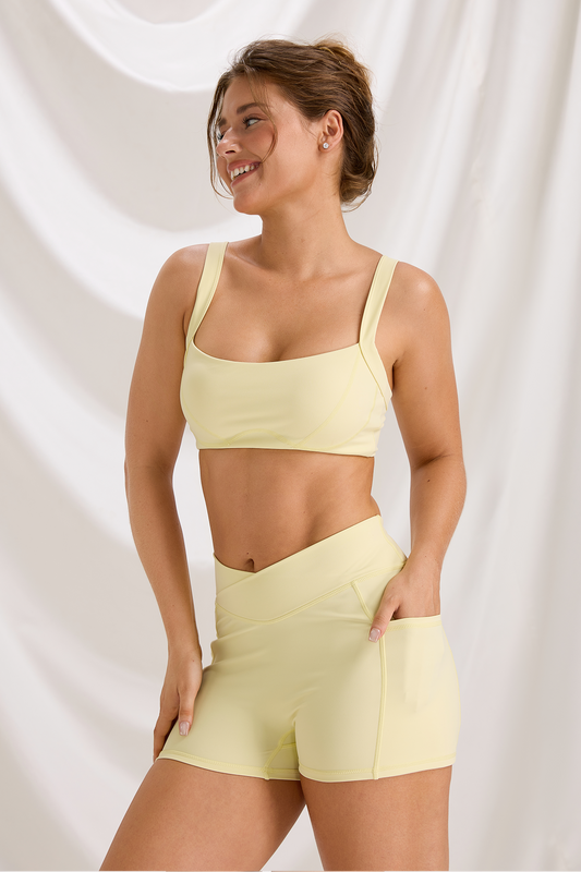 Model wearing the Yellow Curve sports bra and matching high-waisted workout shorts with a crossover waistband