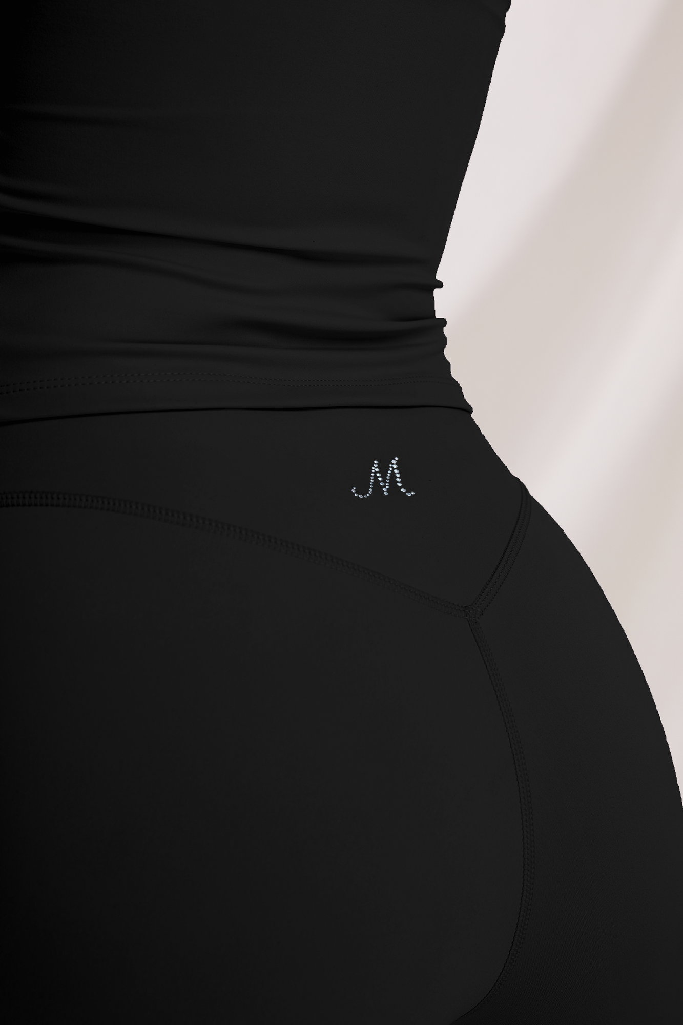 Close-up of black high-waisted workout shorts with Moxy rhinestone M logo at the back waistband
