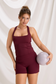 Model holding a Pilates ball while wearing the Burgundy Criss Cross Tank Workout Set
