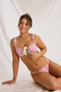 Seated model wearing pink floral mesh underwire bra and matching thong with slim side straps