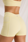 Back detail of yellow high-waisted workout shorts, showing a side pocket, curved seams and M logo