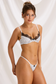Angled front view of ivory polka dot lingerie set with black lace trim and slim thong straps