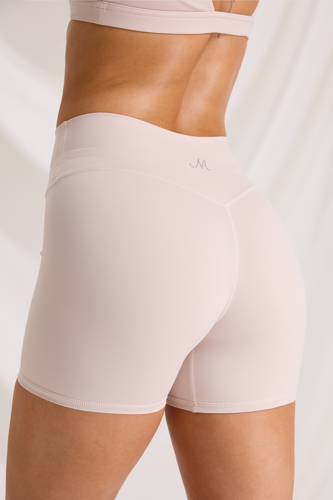 Back close-up of bone-colored workout shorts, showing the high waistband, contoured seams and M logo