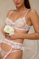 Close up of model wearing pink floral embroidered lingerie bra and matching sheer garter belt with white flowers.